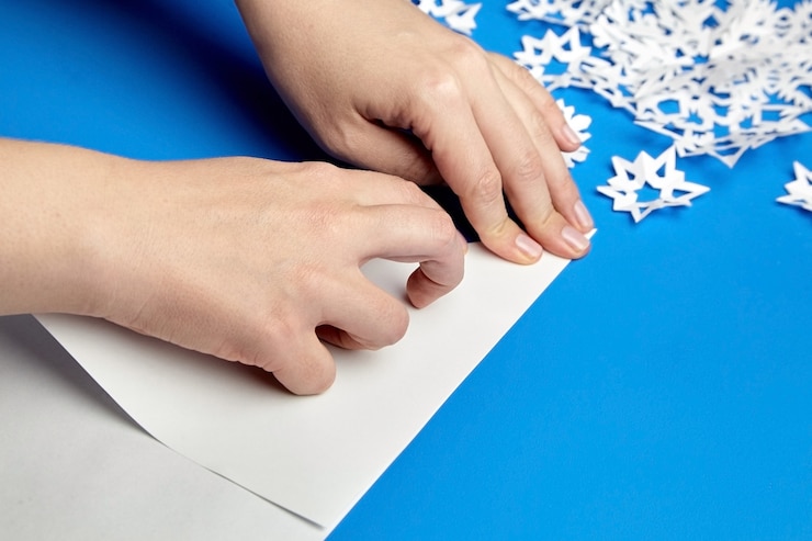 Foto manos haciendo copos de nieve de papel blanco sobre azul