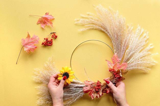 Manos haciendo corona de flores secas de hierba de pampa seca y hojas de otoño.