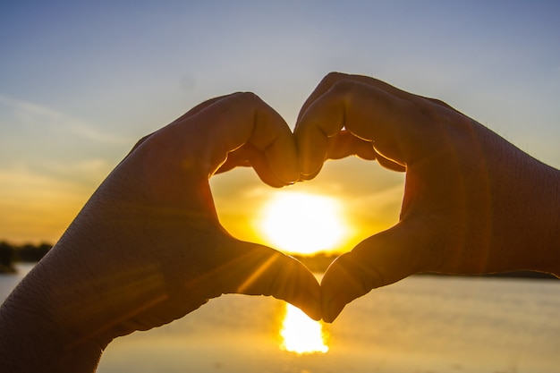 Manos haciendo la forma de un corazón con el sol en el medio.