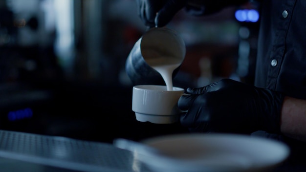 Manos de hombre agregando crema al primer plano de café Camarero haciendo capuchino