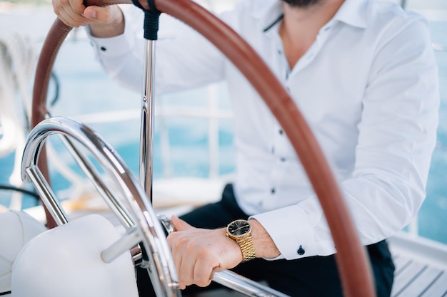 Foto las manos del hombre de camisa blanca sentado al timón en un yate navegando en el medio del mar de cerca