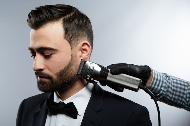 Manos del hombre con camisa haciendo una forma de barba para hombre con cabello negro en el fondo del estudio, retrato, primer plano, recortador, concepto de barbería.