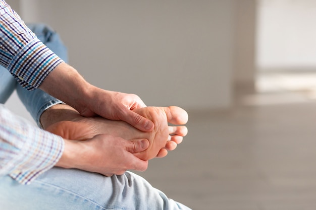 Foto manos de hombre dándose masaje de pies para aliviar el dolor después de una larga caminata, debido a los zapatos incómodos.