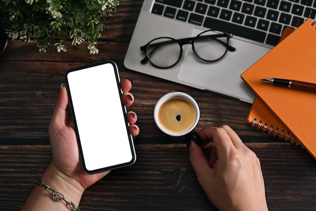 Manos de hombre elegante sosteniendo un teléfono inteligente con pantalla blanca y taza de café