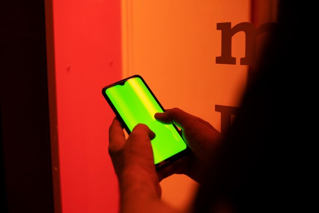 Las manos del hombre escribiendo en la pantalla de un teléfono celular frente a una ventana roja en la noche