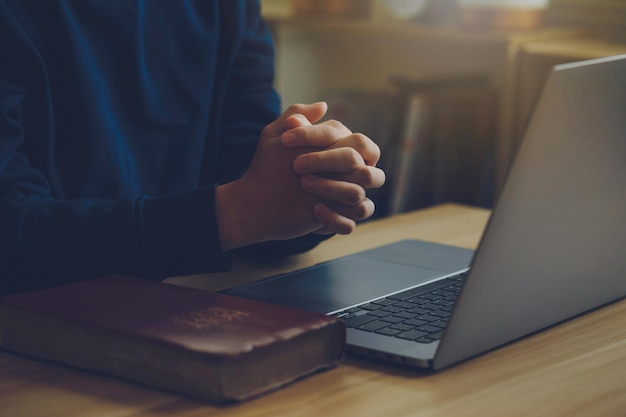 Foto las manos del hombre están cruzadas en oración en una santa biblia sobre un portátil concepto de fe religión amor