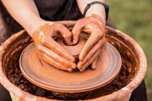 Foto manos del hombre en forma de corazón en arcilla en el molde de la rueda de alfarería jarrón potter trabaja en el taller de alfarería