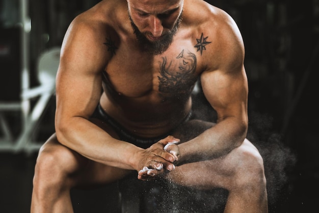 Las manos de un hombre fuerte con talco preparándose para levantar pesas en el gimnasio.