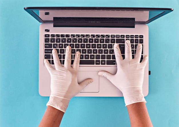 Manos de hombre con guantes de látex escribiendo en el teclado del ordenador portátil