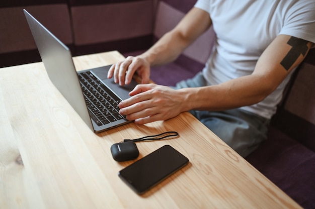 Manos de hombre irreconocibles con teléfono inteligente y auriculares trabajando en una computadora portátil