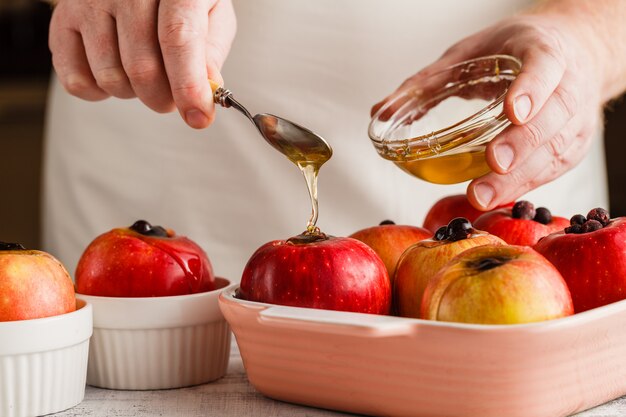 Manos de hombre con miel vertiendo sobre una manzana fresca lista para hornear