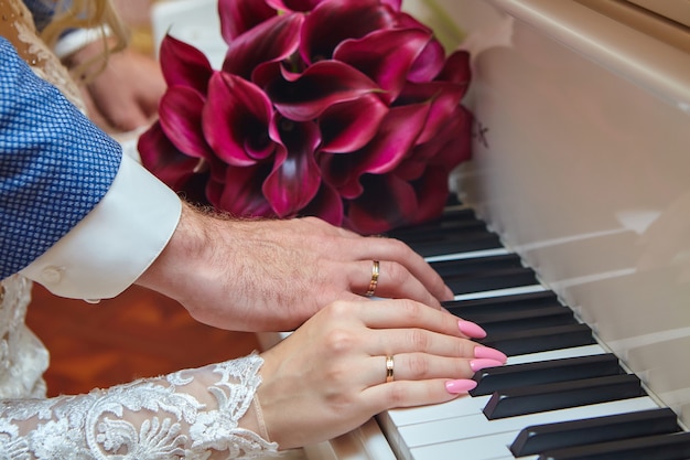 Manos de un hombre y una mujer con anillos de boda en las teclas del piano