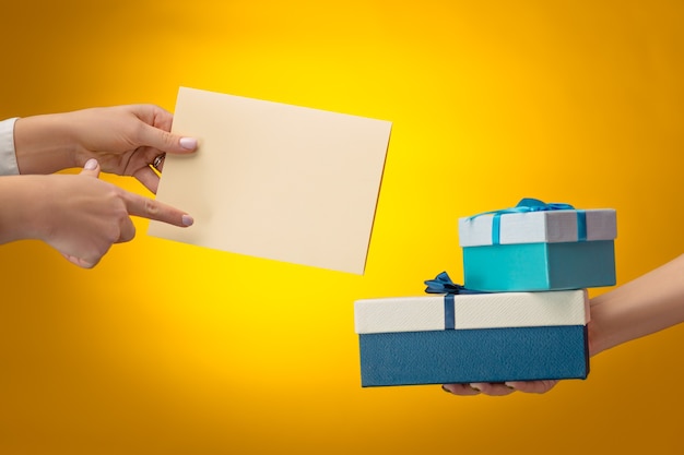 Manos de hombre y mujer con caja de regalo sobre fondo amarillo con espacio de copia en blanco vacío