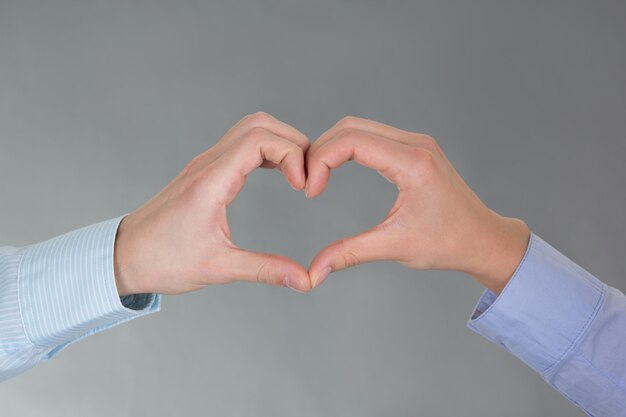 Manos de hombre y mujer formando un corazón sobre gris