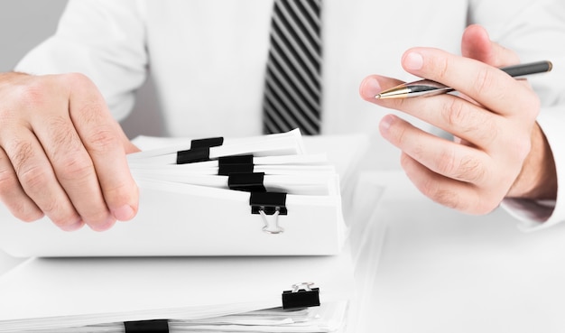 Manos de hombre de negocios trabajando en pilas de archivos en papel para buscar información, negocios y concepto financiero.