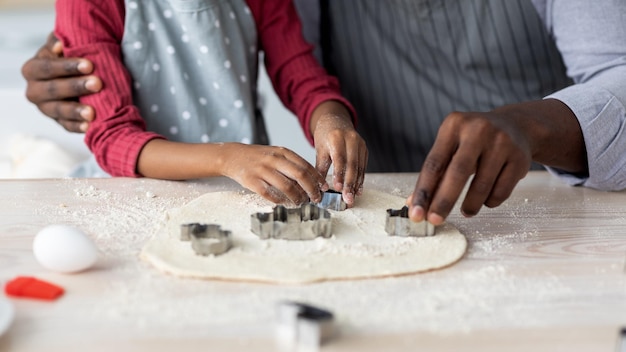 Manos de hombre negro y niño cortando masa para galletas