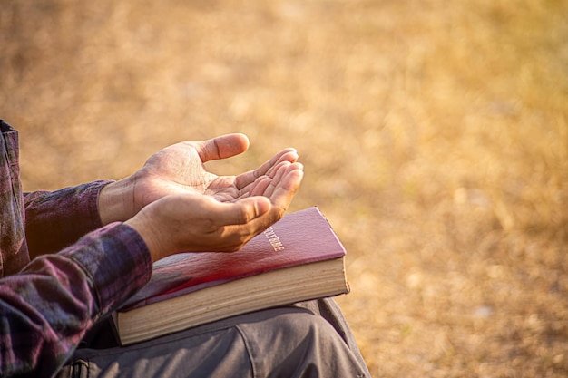 Las manos del hombre orando a Dios con la Biblia Crean en la bondad