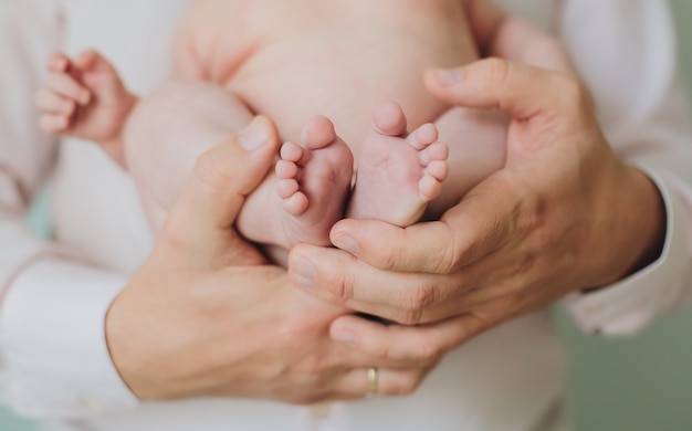 Las manos del hombre del padre sostienen los dedos pequeños de los pies del bebé recién nacido tierna luz colores neutros hermosa familia y papá amor