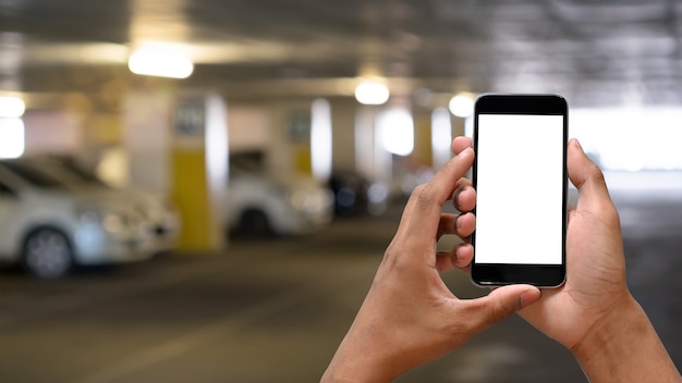 Las manos del hombre con pantalla en blanco de smartphone en el aparcamiento.