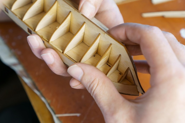 Manos de hombre pegando detalles de madera contrachapada para modelo de barco con pegamento sujetando con los dedos Proceso de construcción de barco de juguete