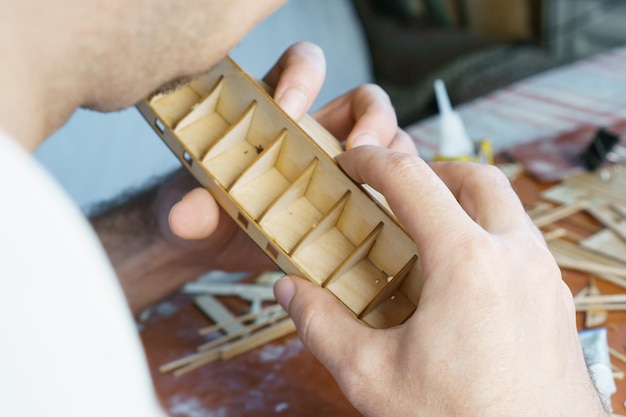 Manos de hombre pegando detalles de madera contrachapada para modelo de barco con pegamento sujetando con los dedos Proceso de construcción de barco de juguete