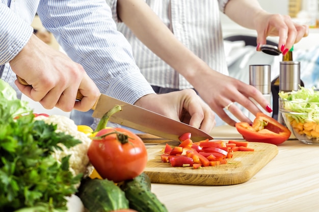 Manos de un hombre picado pimiento rojo para ensalada en una tabla. Par picar verduras en la cocina