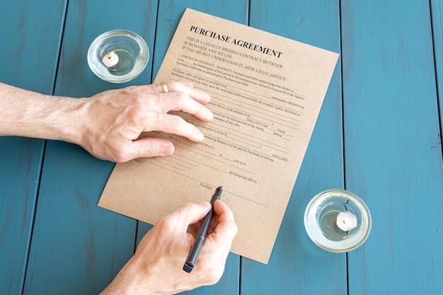 Manos de hombre con pluma estilográfica firmando contrato junto a velas encendidas