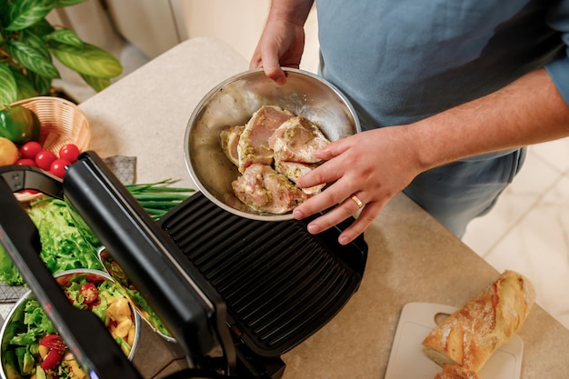Las manos del hombre preparan un delicioso bistec de carne jugosa en una parrilla eléctrica sobre una mesa de madera Humo en la cocina de la casa