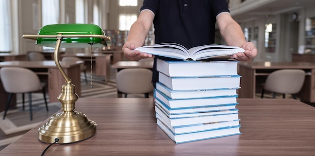 Manos de un hombre que sostiene un libro abierto Pila de libros en el escritorio de madera en la biblioteca