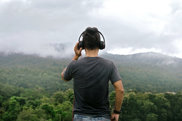 Las manos del hombre que sostienen los auriculares ven detrás. mira a lo lejos con la naturaleza