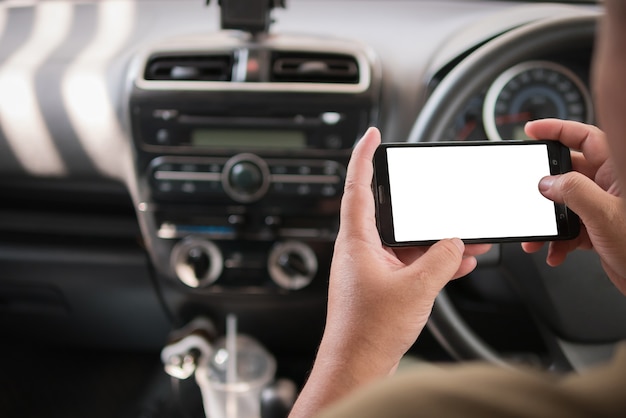 Manos del hombre que usa el teléfono elegante móvil con blanco en blanco para el espacio de la copia en el coche