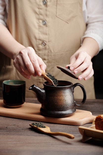 Manos del hombre, remojar el té en una olla de cerámica en la mesa de la cocina