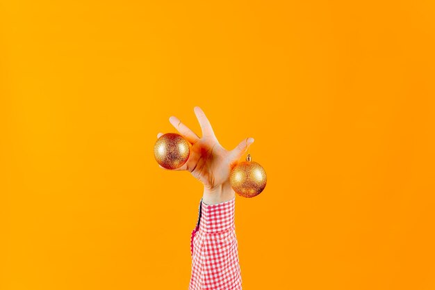 Manos de un hombre sobre un fondo amarillo, que sostienen juguetes de año nuevo, bolas de color dorado