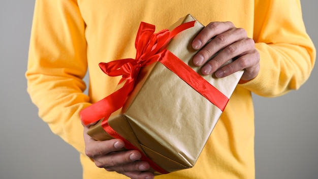 Manos del hombre sosteniendo una caja de regalo con un lazo rojo