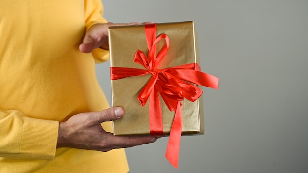 Manos del hombre sosteniendo una caja de regalo con un lazo rojo