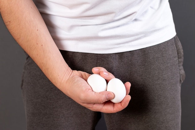 Manos de hombre sosteniendo huevos en la entrepierna media de los pantalones aislados