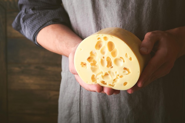 Manos de hombre sostienen dos grandes rebanadas de queso maasdam contra el fondo de la antigua pared de madera en la fábrica de queso Quesero sostiene queso maasdam en la mano Espacio libre para su texto