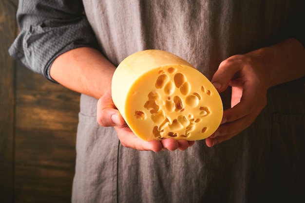Manos de hombre sostienen dos grandes rebanadas de queso maasdam contra el fondo de la antigua pared de madera en la fábrica de queso Quesero sostiene queso maasdam en la mano Espacio libre para su texto
