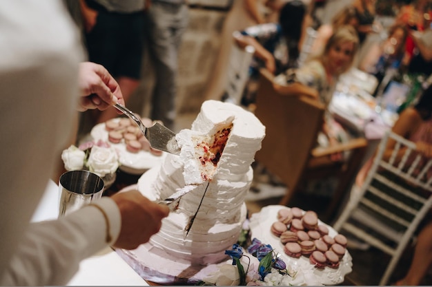 Las manos del hombre sostienen un trozo de pastel de bodas con un cuchillo y una espátula