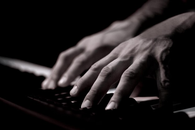 Foto las manos de un hombre tatuado en el teclado de un piano de fondo oscuro