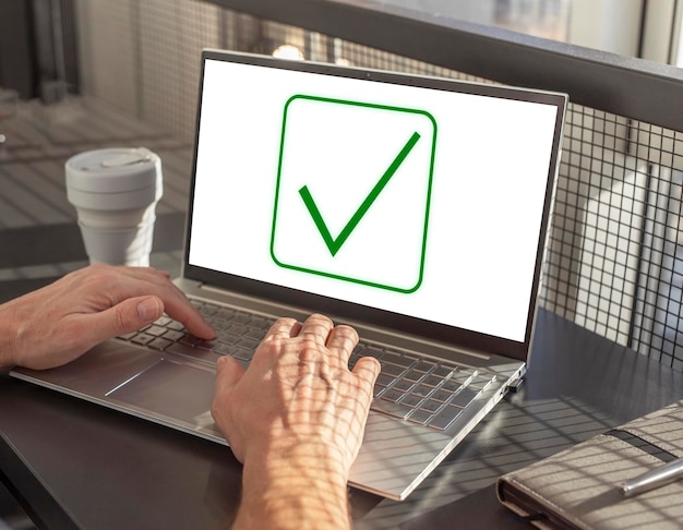 Manos del hombre en el teclado de la computadora portátil y el ícono de marca en la pantalla Aprobación de la verificación de un proyecto o confirmación de datos Hombre sentado en la mesa con una computadora portátil y una taza para llevar