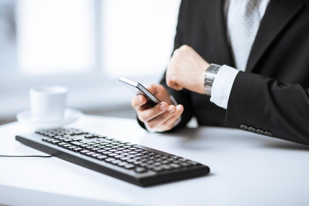 manos de hombre con teclado viendo el tiempo y sosteniendo el teléfono inteligente