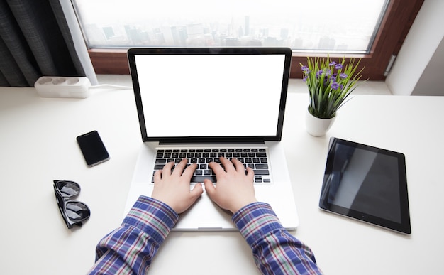 Manos del hombre usando una computadora portátil con pantalla en blanco junto a una ventana de la ciudad