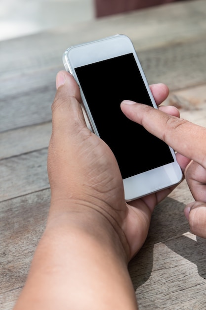 las manos del hombre usando el teléfono inteligente en la mesa de madera