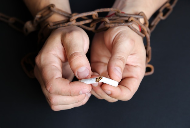 Foto las manos del hombre en viejas cadenas oxidadas cerca del cigarrillo. adicto a fumar. hábito peligroso.