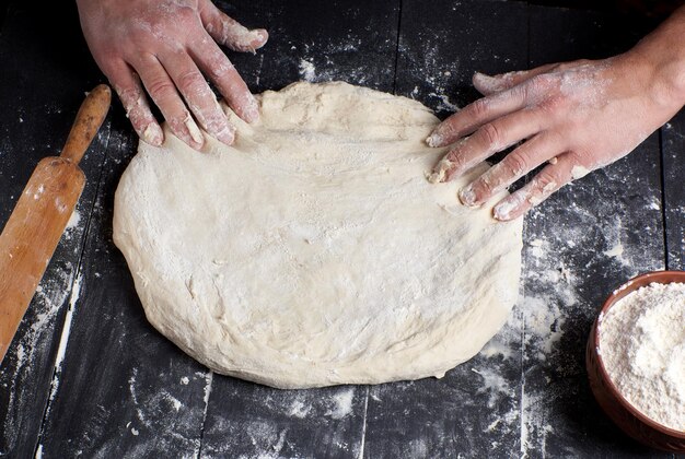 las manos de los hombres amasan una pieza redonda de masa para hacer pizza vista superior