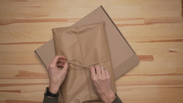 Foto las manos de los hombres empaquetan el paquete en papel artesanal y lo colocan en una caja de papel marrón contra una mesa de madera