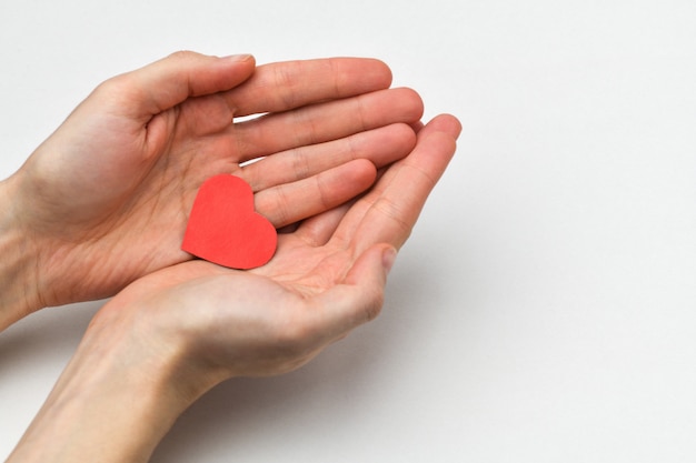 En las manos de los hombres se encuentra un pequeño corazón rojo sobre un fondo gris. Un fragmento de las manos de un hombre.