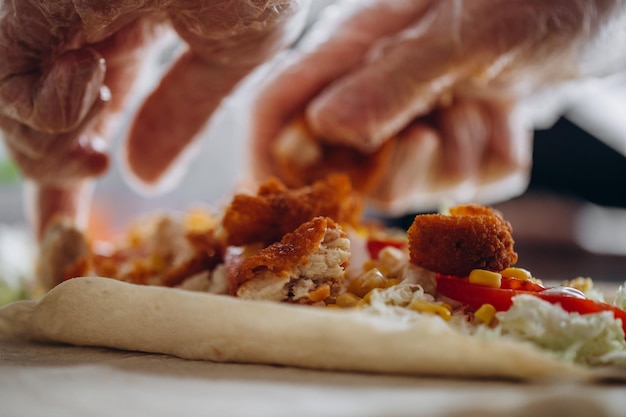 Manos de hombres envolviendo envoltura tradicional de shawarma con pollo y verduras