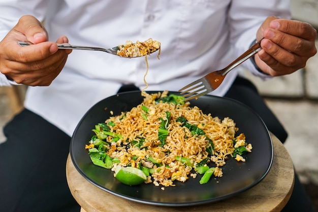 Las manos de los hombres están comiendo puré de cuchara Thai Pat frito de fideos y verduras en plato negro